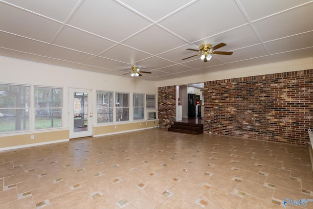 unfurnished living room featuring ceiling fan, brick wall, and a drop ceiling