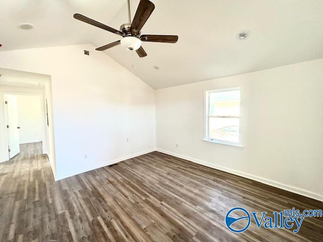 empty room with dark wood-style floors, vaulted ceiling, a ceiling fan, and baseboards