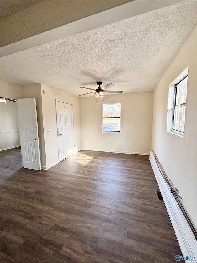 unfurnished bedroom featuring ceiling fan, dark hardwood / wood-style flooring, multiple windows, and a textured ceiling