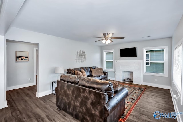 living area featuring baseboards, a ceiling fan, dark wood-style floors, and a wealth of natural light