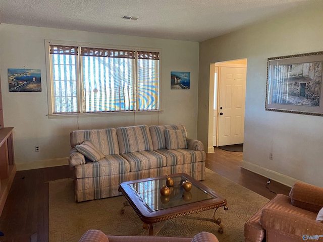 living area with baseboards, a textured ceiling, visible vents, and wood finished floors