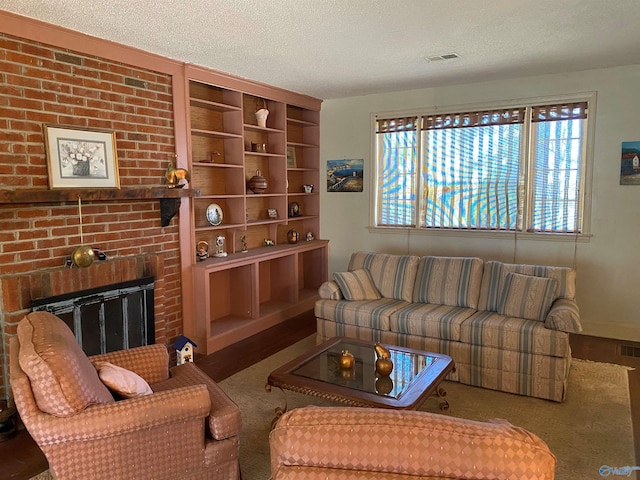 living room featuring a brick fireplace, wood finished floors, a textured ceiling, and visible vents
