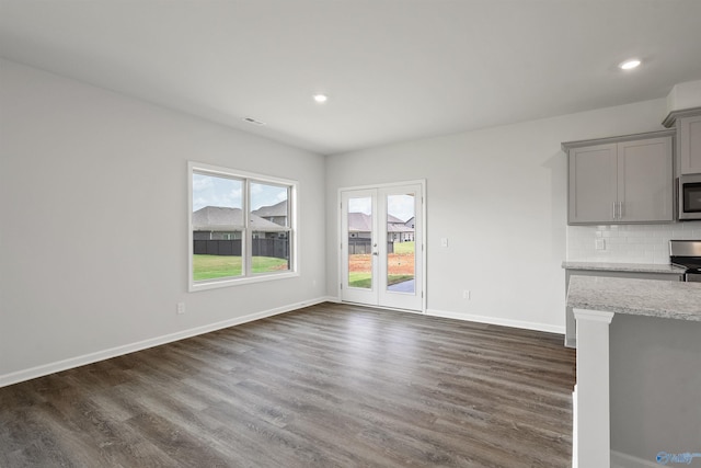 kitchen featuring gray cabinetry, backsplash, light stone countertops, appliances with stainless steel finishes, and dark hardwood / wood-style flooring