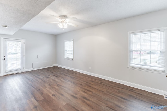 empty room featuring a textured ceiling, dark hardwood / wood-style floors, and a healthy amount of sunlight