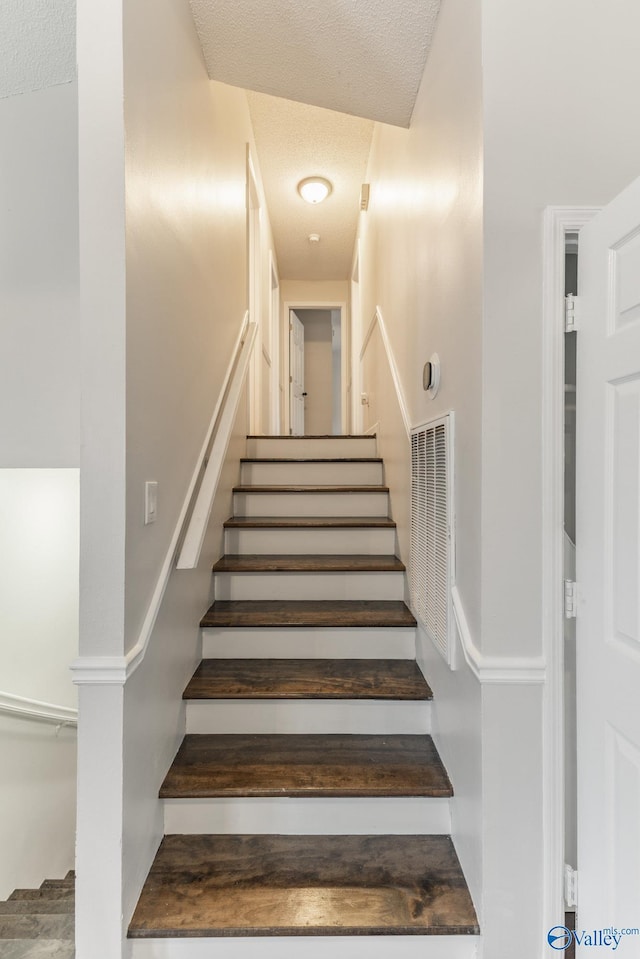 stairway with visible vents and a textured ceiling