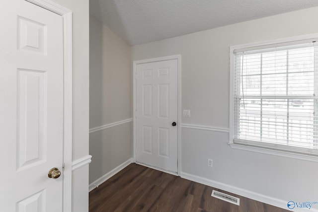 unfurnished room with a textured ceiling, plenty of natural light, and dark wood-type flooring