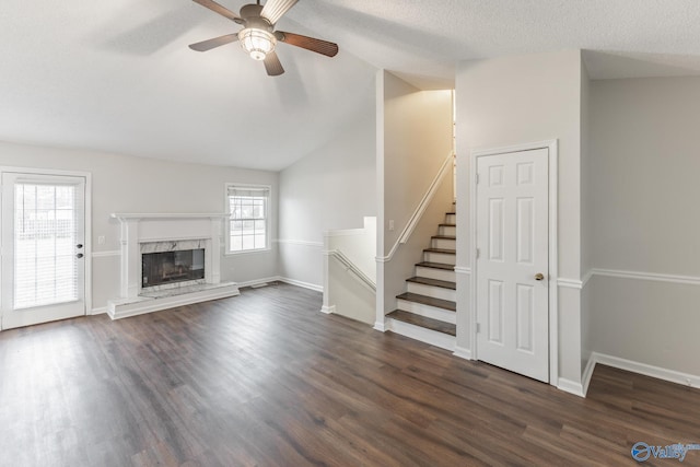 unfurnished living room with dark wood-type flooring, a high end fireplace, vaulted ceiling, ceiling fan, and a textured ceiling