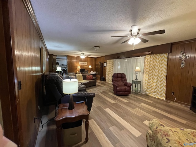 living room with ceiling fan, light wood-type flooring, a textured ceiling, and wood walls