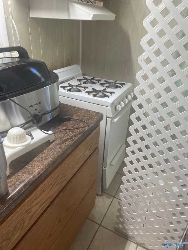 kitchen featuring light tile patterned flooring, dark stone countertops, and white range with gas stovetop