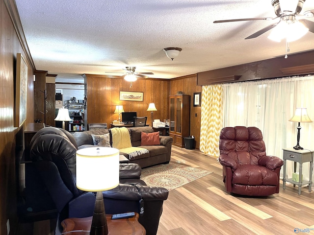 living room featuring ceiling fan, wood walls, a textured ceiling, and light wood-type flooring