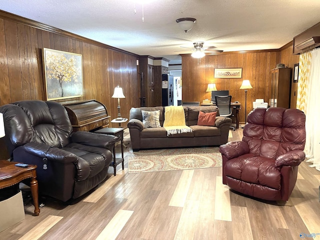 living room featuring crown molding, light hardwood / wood-style flooring, ceiling fan, wooden walls, and a textured ceiling