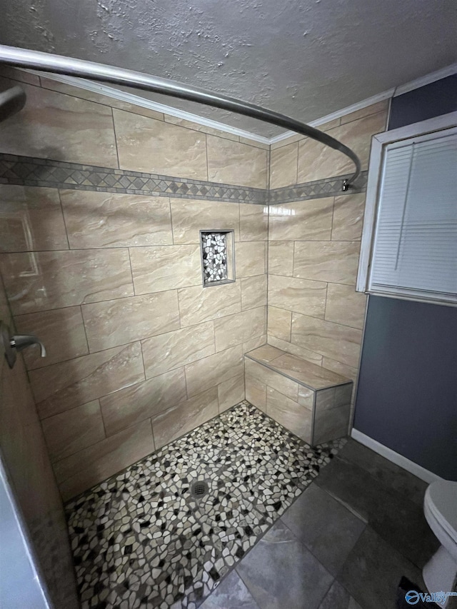 bathroom with baseboards, a textured ceiling, toilet, and tiled shower