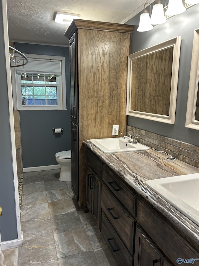 bathroom featuring a sink, double vanity, toilet, stone finish floor, and baseboards