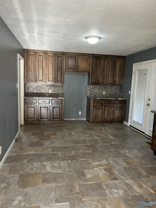 kitchen featuring baseboards, decorative backsplash, and stone finish flooring