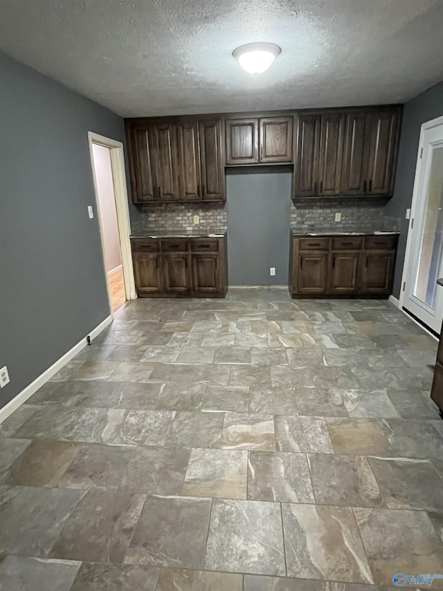 kitchen with baseboards, a textured ceiling, backsplash, and stone finish floor