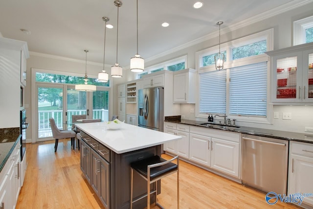 kitchen with white cabinets, ornamental molding, stainless steel appliances, light wood-type flooring, and a sink