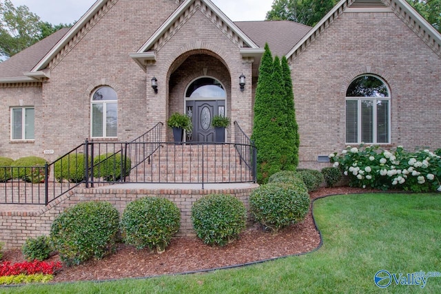 view of front of property featuring a shingled roof, a front yard, and brick siding