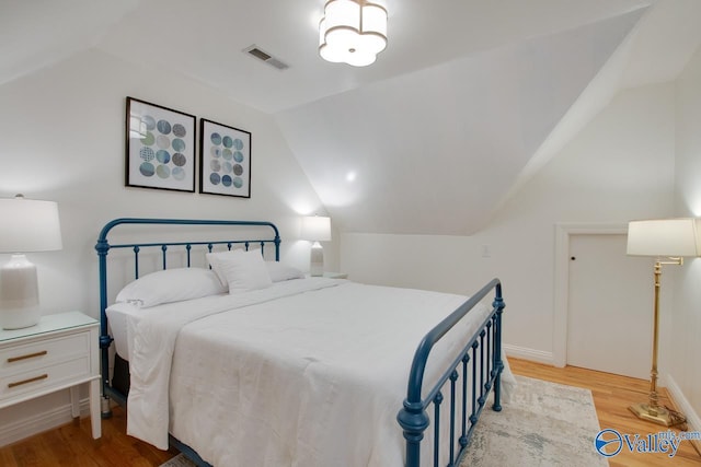 bedroom featuring light wood-style floors, baseboards, visible vents, and vaulted ceiling