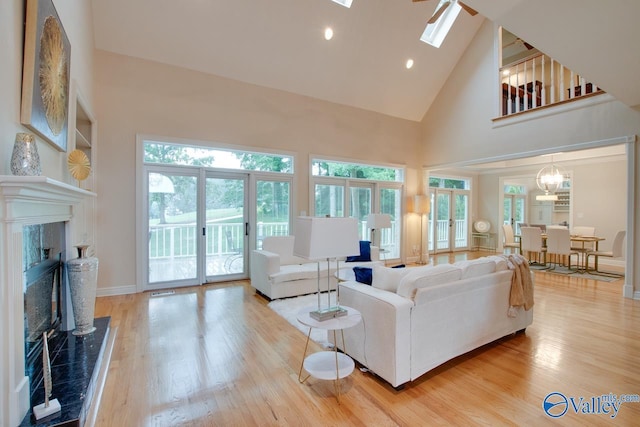 living area with light wood finished floors, a skylight, baseboards, a premium fireplace, and high vaulted ceiling