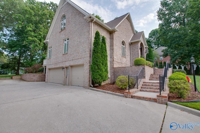 view of side of home with stairs, driveway, brick siding, and a garage