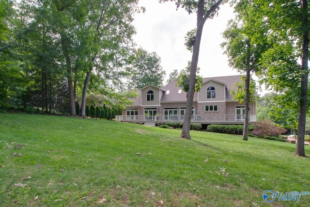 rear view of property featuring a deck, brick siding, and a lawn