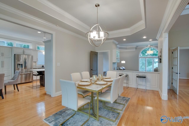 dining area with light wood finished floors, a raised ceiling, crown molding, and an inviting chandelier