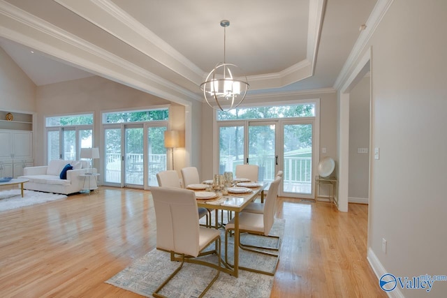 dining area featuring light wood-style floors, a tray ceiling, crown molding, and plenty of natural light