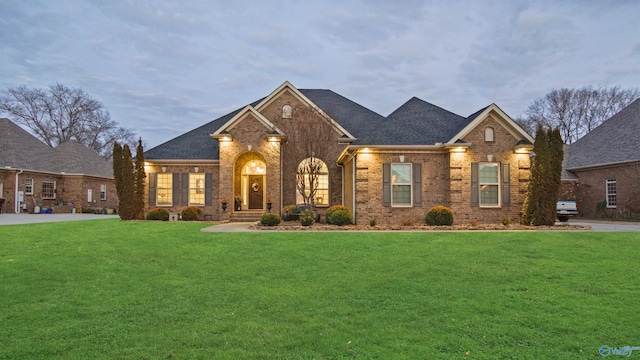 view of front of home with roof with shingles, a front lawn, and brick siding