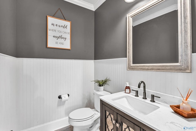 half bathroom featuring ornamental molding, wainscoting, vanity, and toilet