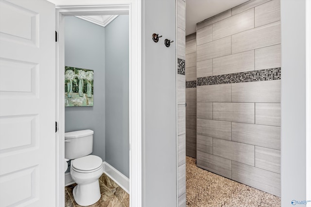 bathroom featuring ornamental molding, a tile shower, toilet, and baseboards