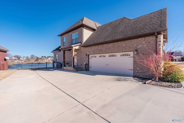 view of side of property with brick siding, a shingled roof, concrete driveway, an attached garage, and a gate