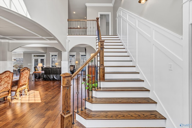 staircase with arched walkways, wainscoting, hardwood / wood-style flooring, ornamental molding, and a decorative wall