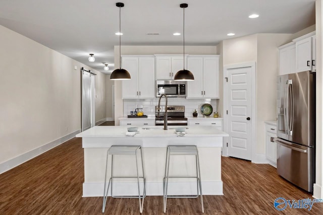 kitchen featuring stainless steel appliances, white cabinets, a barn door, and an island with sink