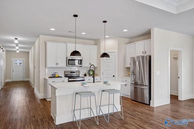 kitchen featuring stainless steel appliances, decorative light fixtures, white cabinetry, a kitchen island with sink, and a breakfast bar