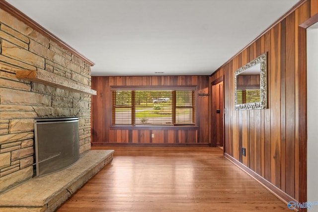 unfurnished living room with a stone fireplace, wood walls, and hardwood / wood-style floors