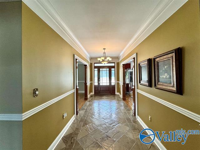 doorway to outside featuring baseboards, a chandelier, stone tile floors, and ornamental molding