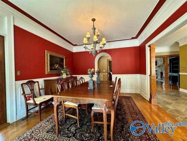 dining area featuring a wainscoted wall, crown molding, a fireplace, an inviting chandelier, and wood finished floors