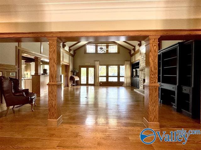 unfurnished living room featuring a large fireplace, wood finished floors, ornate columns, high vaulted ceiling, and beam ceiling