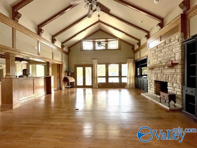 unfurnished living room with beam ceiling, ceiling fan, a stone fireplace, and wood finished floors