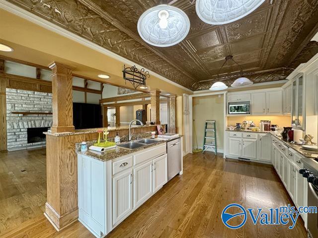 kitchen featuring a sink, white cabinetry, appliances with stainless steel finishes, wood-type flooring, and an ornate ceiling