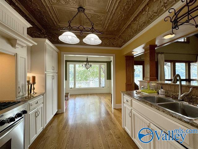 kitchen featuring an ornate ceiling, wood finished floors, a sink, white cabinets, and stainless steel range with gas stovetop