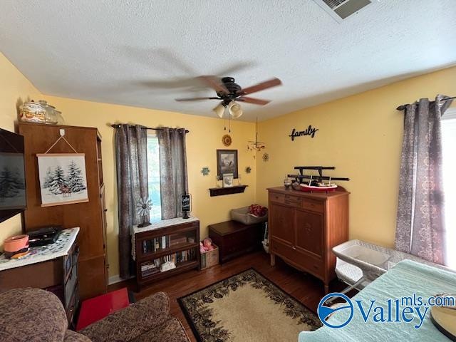 living room with a textured ceiling, ceiling fan, and dark wood-type flooring