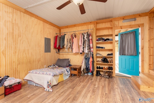 bedroom with wood walls, wood-type flooring, electric panel, and ceiling fan