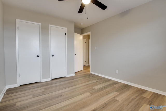 unfurnished bedroom with ceiling fan, light hardwood / wood-style floors, and multiple closets