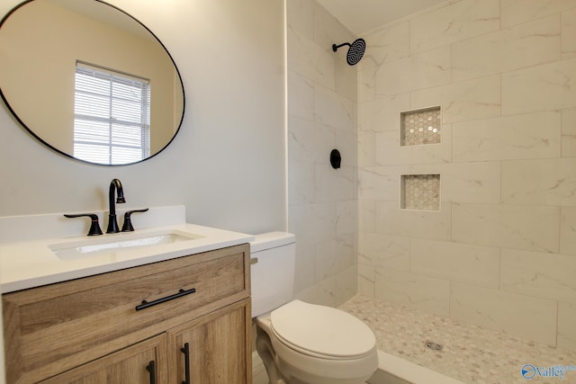 bathroom with toilet, tiled shower, and vanity