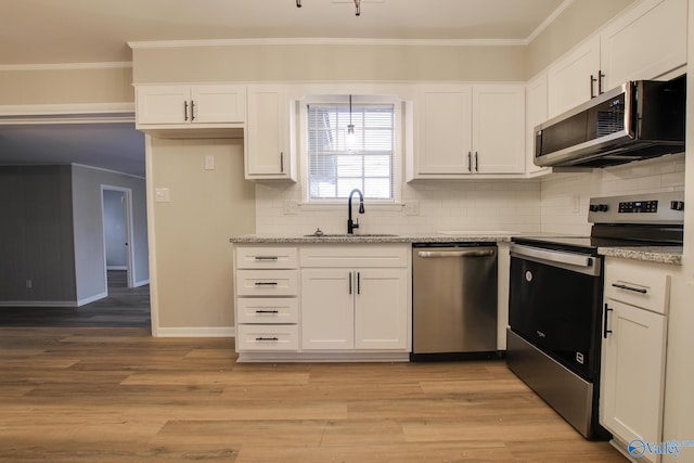 kitchen with appliances with stainless steel finishes, white cabinetry, sink, light stone counters, and light hardwood / wood-style flooring