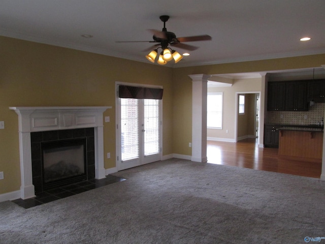 unfurnished living room with ceiling fan, dark carpet, a tile fireplace, and crown molding