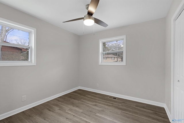 empty room featuring a healthy amount of sunlight, ceiling fan, and dark wood-type flooring