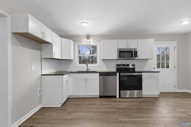 kitchen featuring appliances with stainless steel finishes, light wood-type flooring, a healthy amount of sunlight, white cabinets, and sink