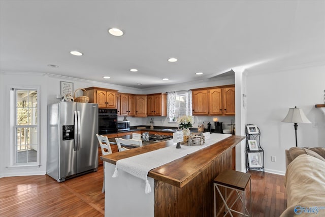 kitchen featuring wood finished floors, appliances with stainless steel finishes, ornamental molding, and brown cabinets